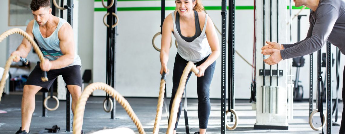 Fitness gym with man and woman working out with battle ropes at the gym with trainer