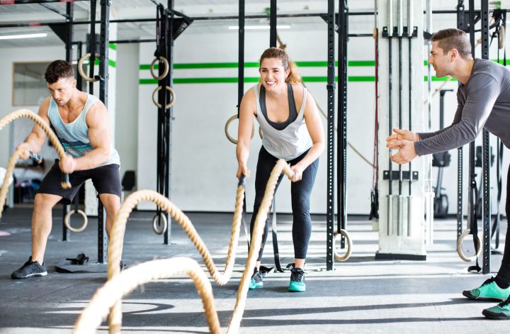 Fitness gym with man and woman working out with battle ropes at the gym with trainer